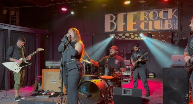 Second Illusion drummer performing live behind drum kit, focused mid-performance under pink and red lighting at BFE Rock Club.